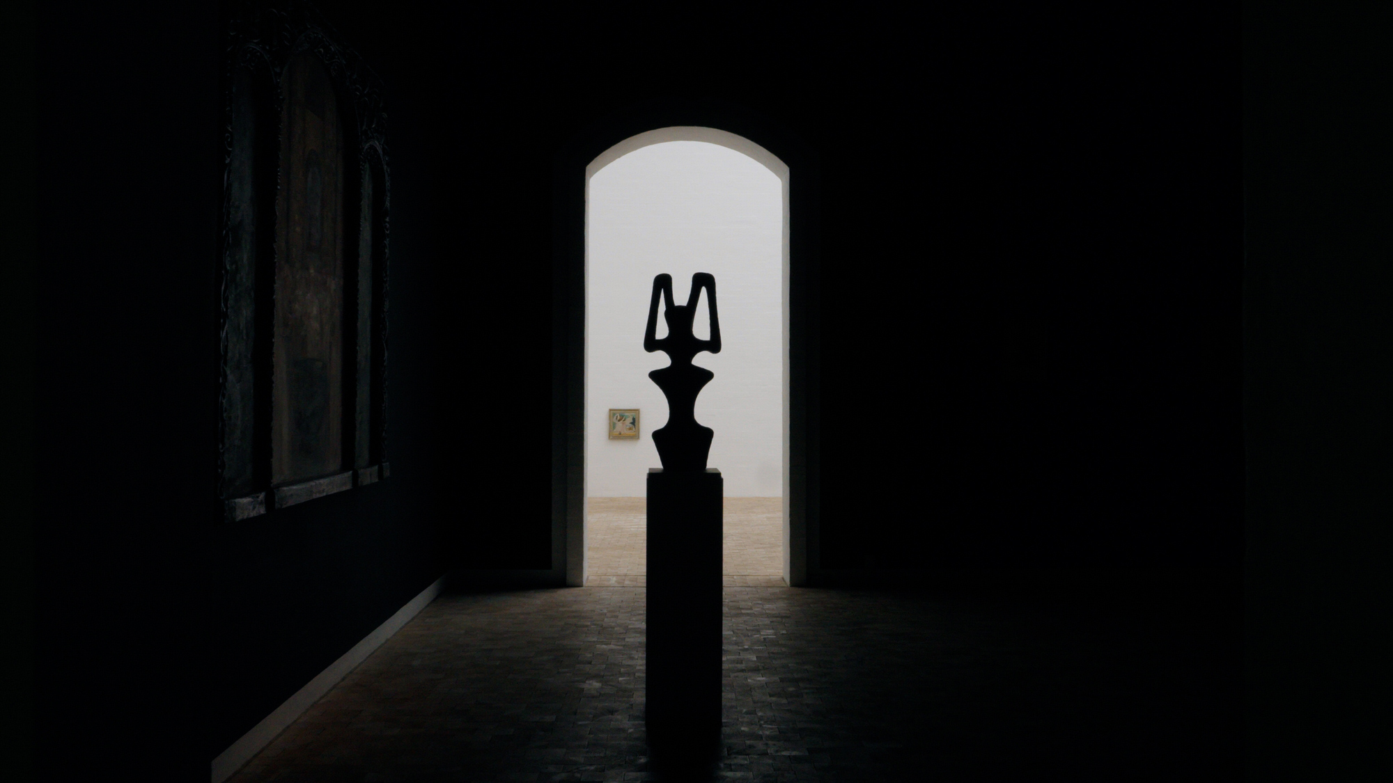 A sculpture on a plinth seen through a dark doorway